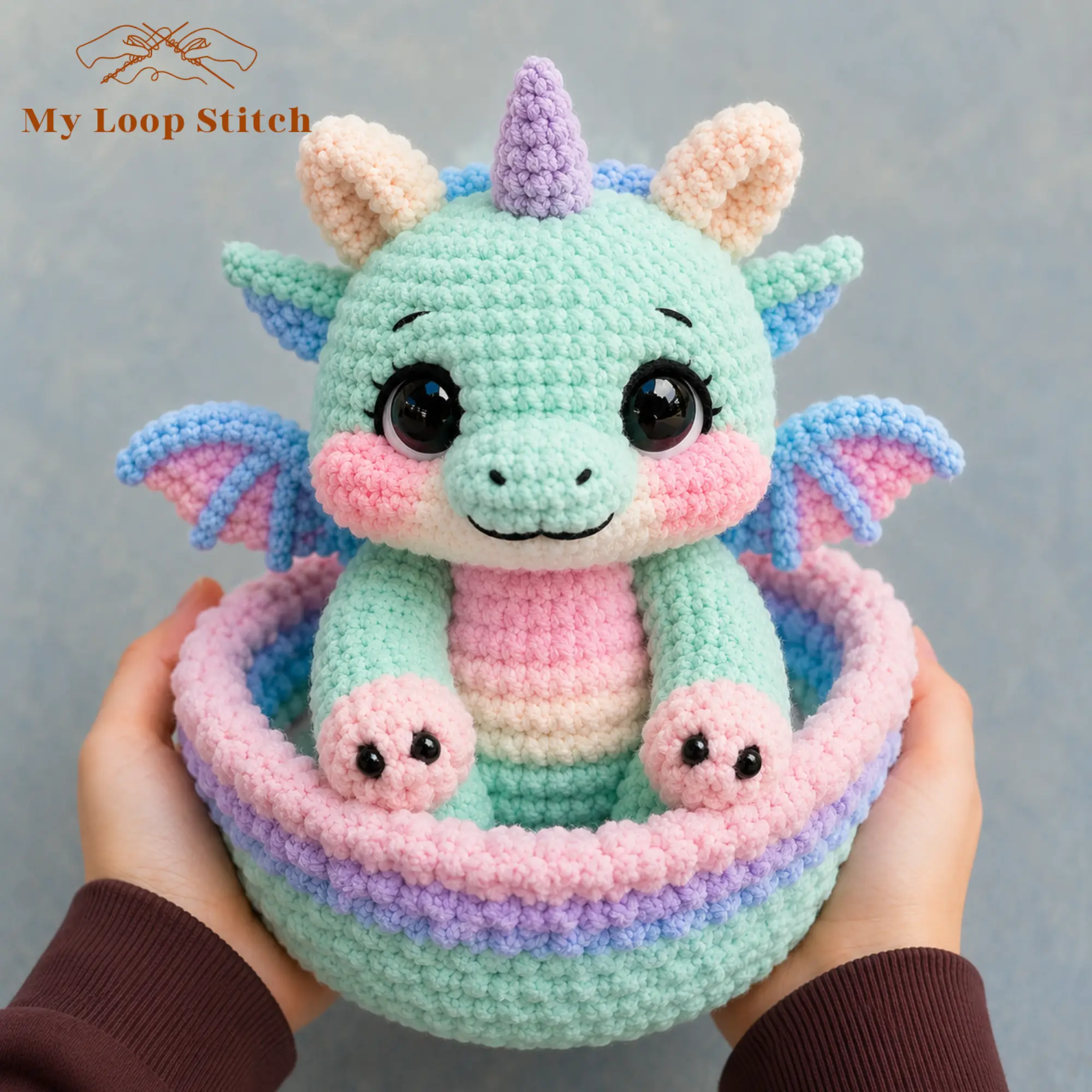 Dragon Amigurumi Pattern PDF – Pastel Baby Dragon in a Basket Close-up of pastel crochet baby dragon with large black eyes, blue-and-pink wings, pink paws and mint-green basket